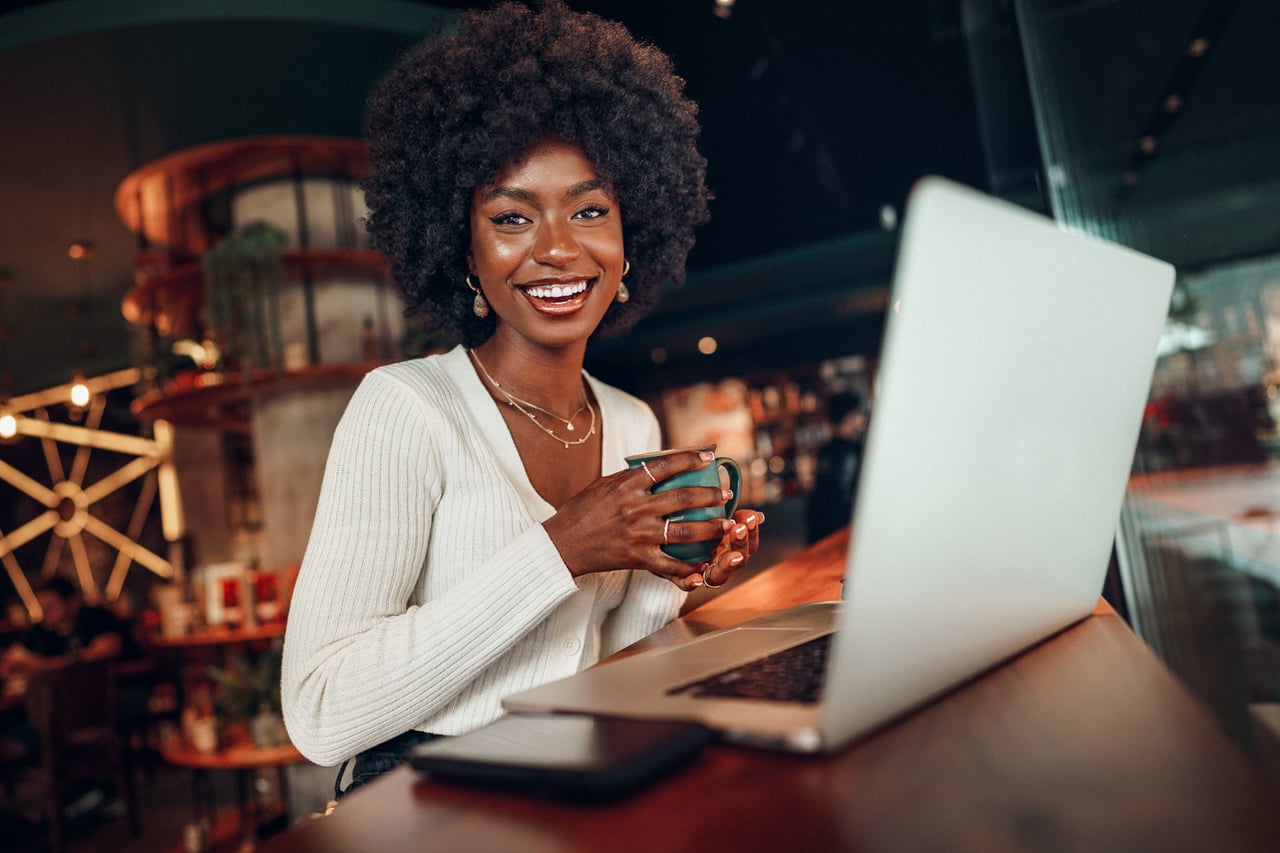 Person holding a coffee mug while using laptop at a coffee shop.