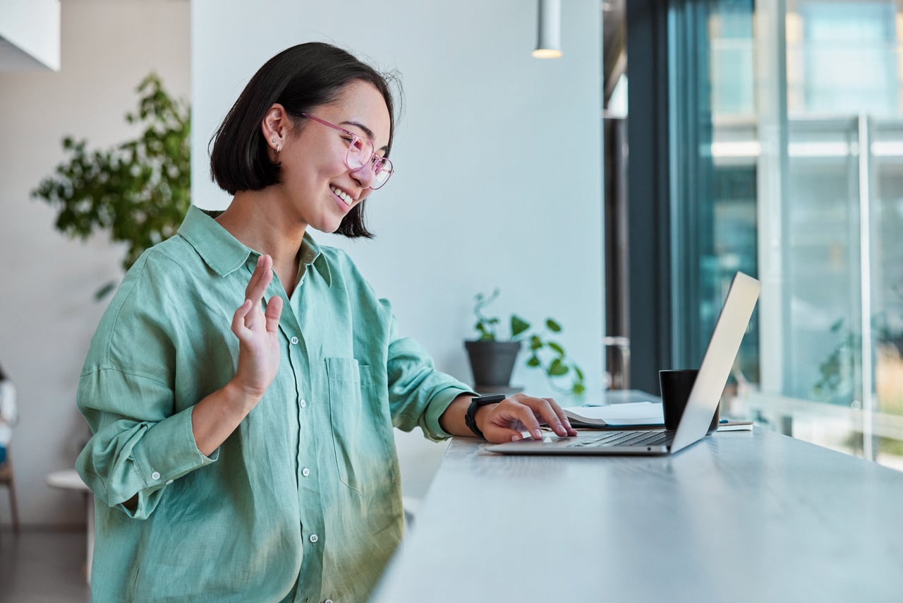 Student waving at laptop screen during online class