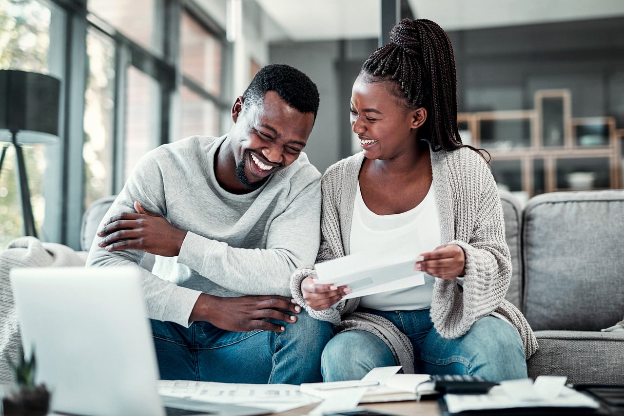Two people talking together on a couch while reviewing paperwork.
